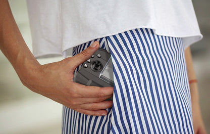 Person wearing blue and white striped shorts with a white shirt, holding a camera.